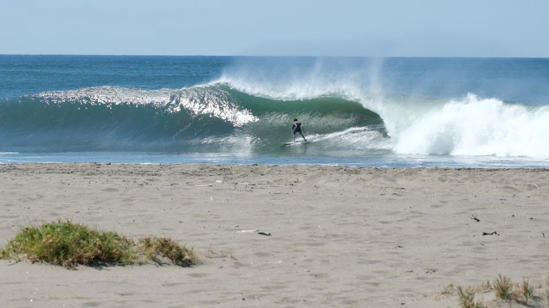 A surfer tucked inside a hollow green wave, with the sand of the beach in the foreground
